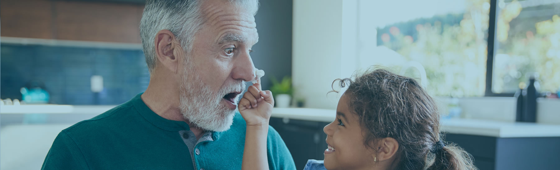 Grandchild putting frosting on grandfather's nose, while smiling